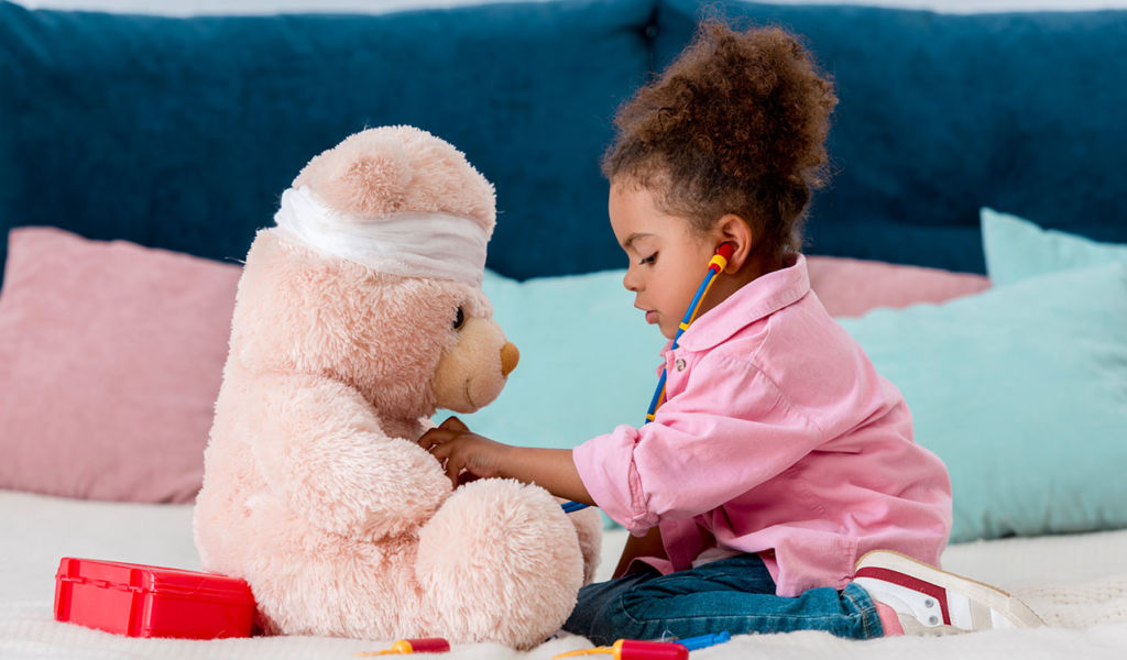 child in pink jacket playing the doctor with teddy bear